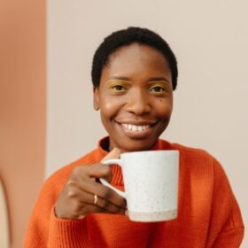Smiling woman holding a white speckled mug and wearing an orange sweater