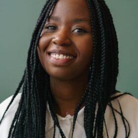 Smiling woman with long braided hair wearing a white top in front of a green background